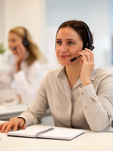 Kundendienstmitarbeiterin am Telefon mit Notizblock in einem hellen Servicebereich